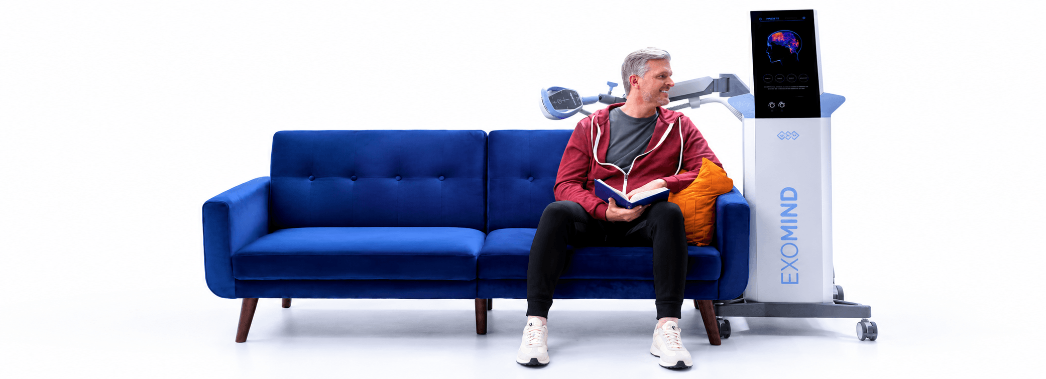 Man reading on a blue sofa next to an Exomind rTMS device at Victoria Memory Clinic